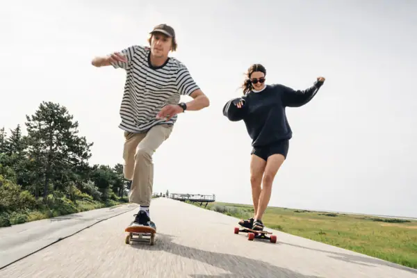 Zwei Menschen fahren auf Longboards über Asphalt.