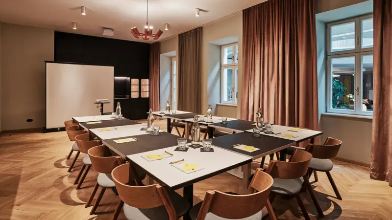 Ein Raum mit Tischen in U-Form, mehreren Stühlen und einer Leinwand im Hintergrund.
