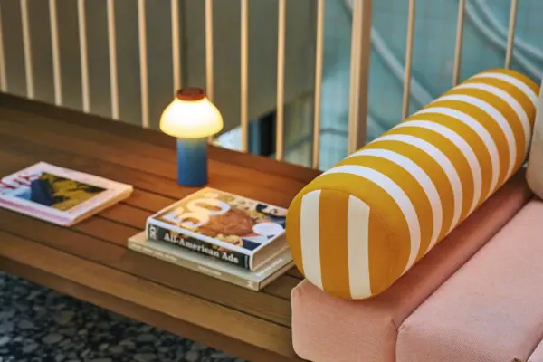 Detailaufnahme einer Design-Sitzbank mit gestreifter Rolle, stilvoller Tischleuchte und Lifestyle-Magazinen im modernen Loungebereich