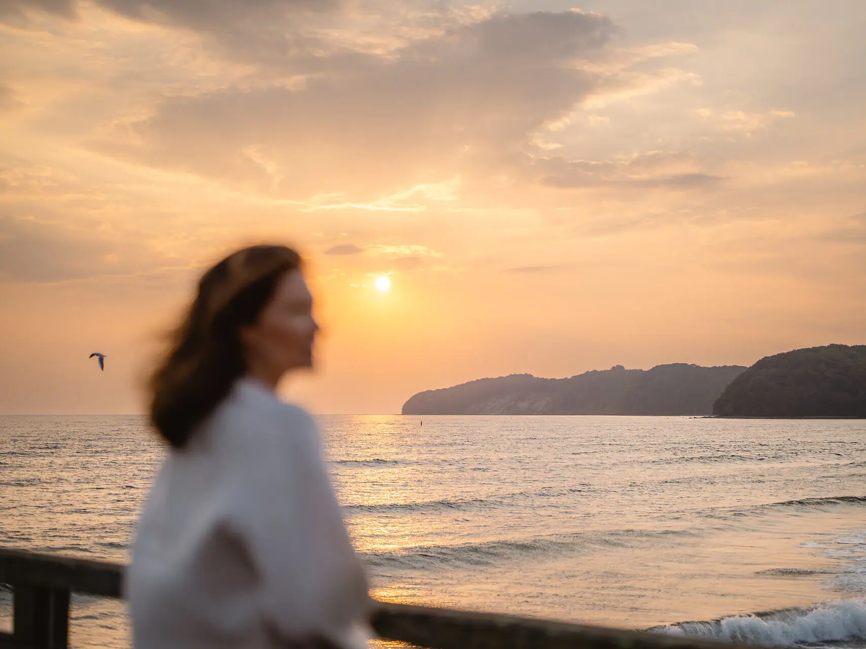 Eine Frau steht an einem Strand bei Sonnenuntergang.