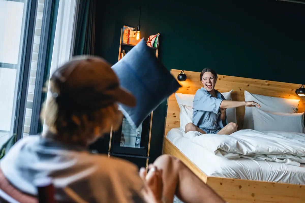 Eine Frau sitzt auf einem Bett und wirft ein Kissen in die Luft.