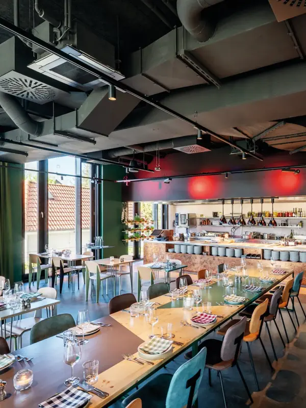 Ein Restaurant mit vielen Tischen sowie einer langen Tafel, die mit Tellern und Gläsern gedeckt sind.