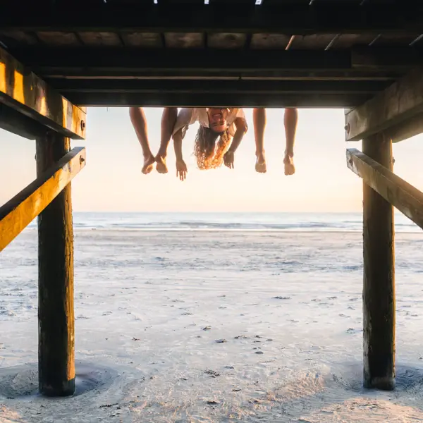 Eine Gruppe von Menschen lassen ihre Füße von den Pfahlbauten am Strand von St. Peter-Ording baumeln.