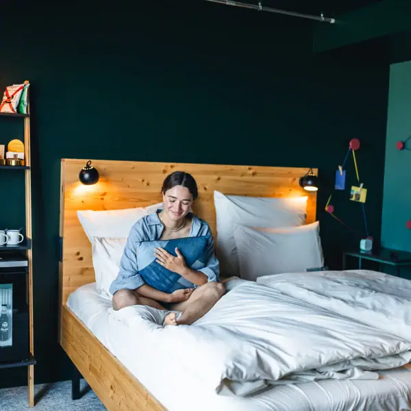 Zimmer im Urban Nature St. Peter-Ording Eine Frau sitzt auf einem Bett in einem Zimmer im Urban Nature Hotel St. Peter-Ording und hält ein Kissen in ihren Armen.