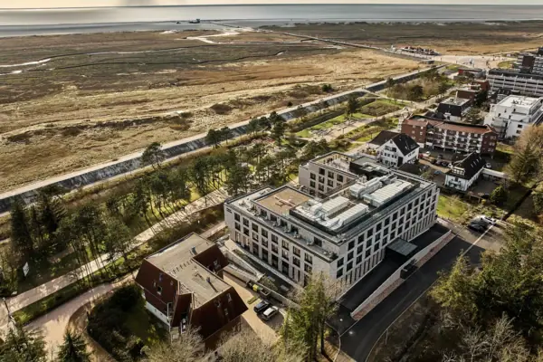 Urban Nature Hotel St. Peter-Ording Das Urban Nature Hotel St. Peter-Ording neben dem Deich aus der Vogelperspektive und der Nordsee im Hintergrund.
