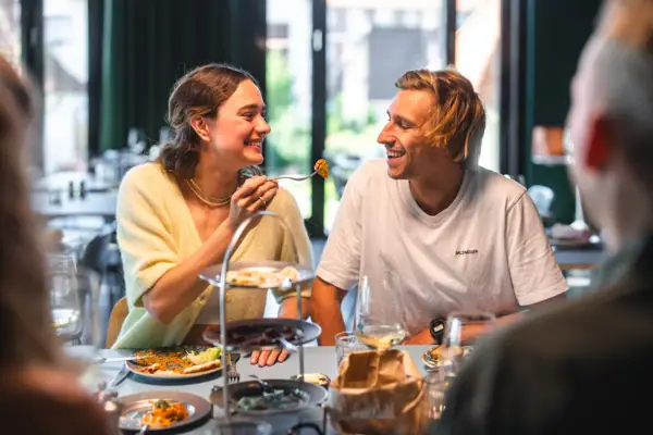 Eine Frau hebt eine Gabel an den Mund eines Mannes in einem Restaurant.