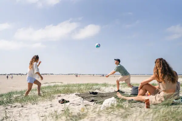 Eine Gruppe von Personen am Strand von St. Peter-Ording spielt mit einem Beachvolleyball.