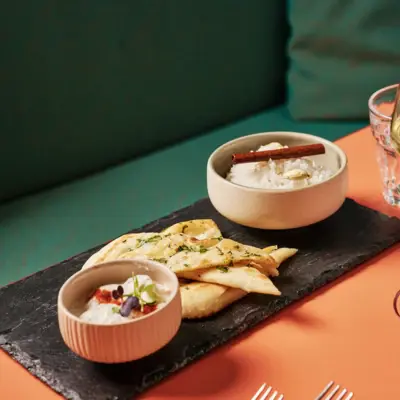 Eine Vorspeise mit Brot und Dips ist auf einem Schieferbrett angerichtet.