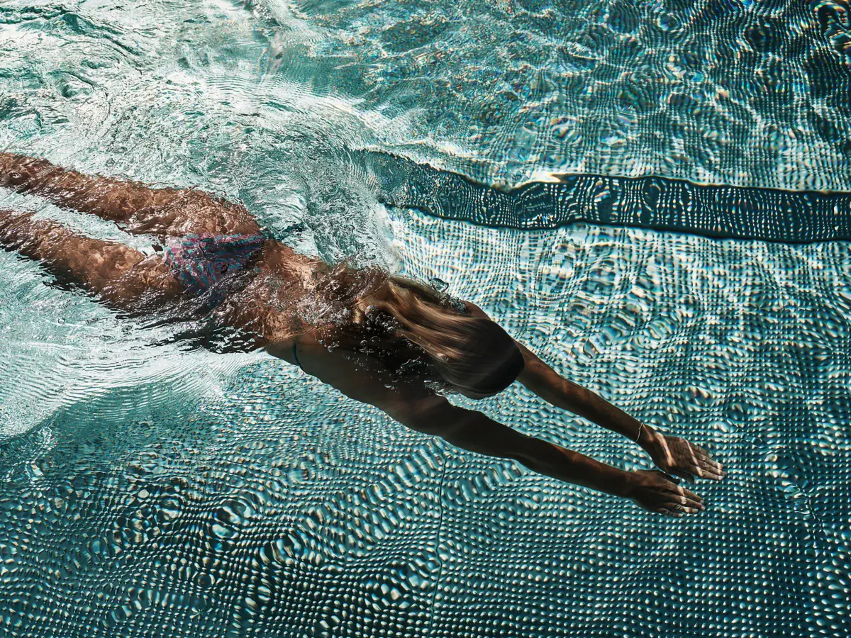 Eine Frau taucht durch einen hellblauen Pool.