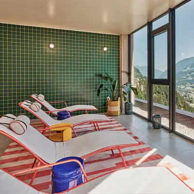 Heller Ruheraum mit stylischen Liegen, farbenfroher Einrichtung und Panoramafenster mit Blick auf die Berge von Bad Gastein