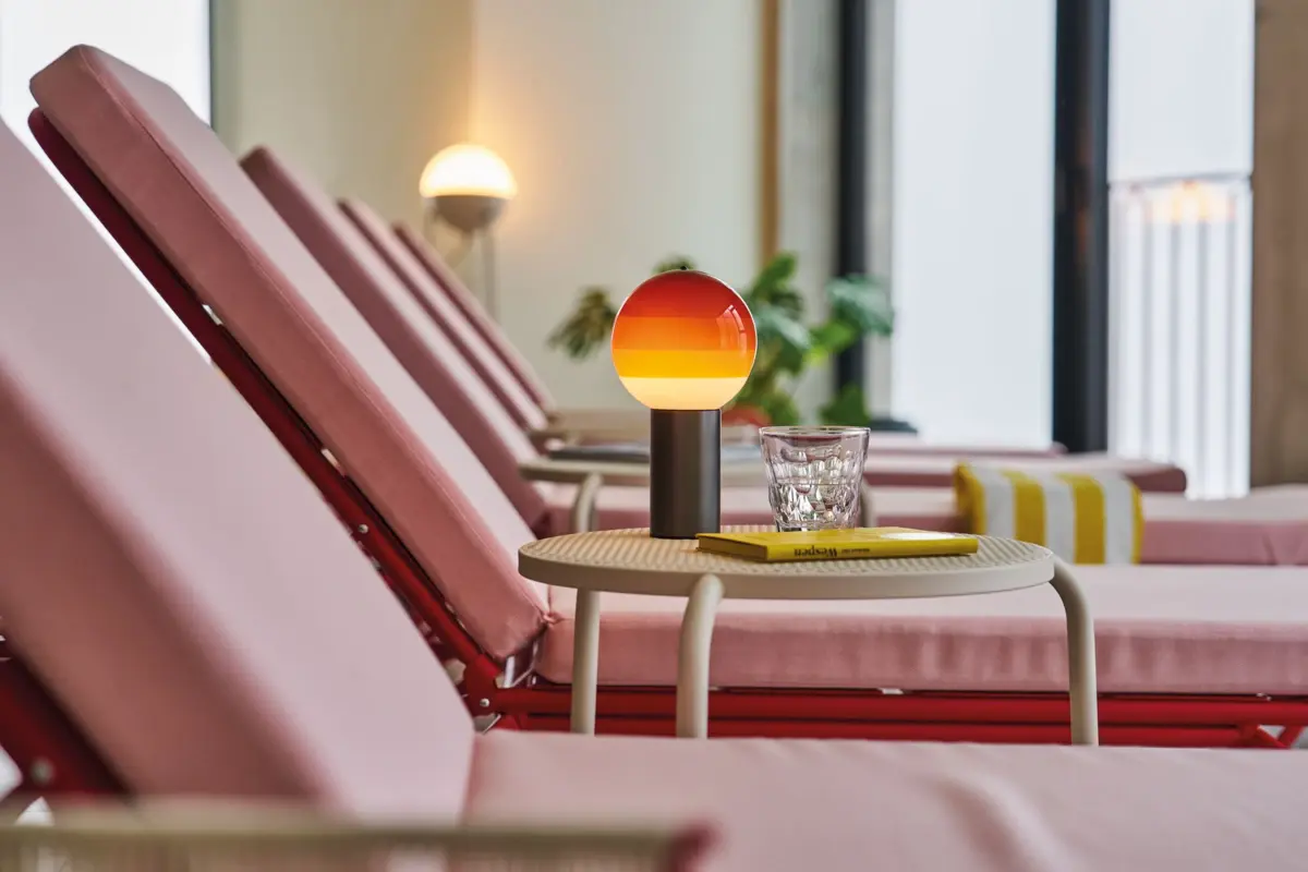 Ruheraum im Alpine Swim Club Reihe rosa Liegen mit Beistelltisch, Glas Wasser und stylischer Lampe in Sonnenuntergangsfarben