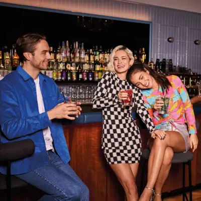 Drei junge Erwachsene genießen bunte Cocktails an einer stilvollen Hotelbar