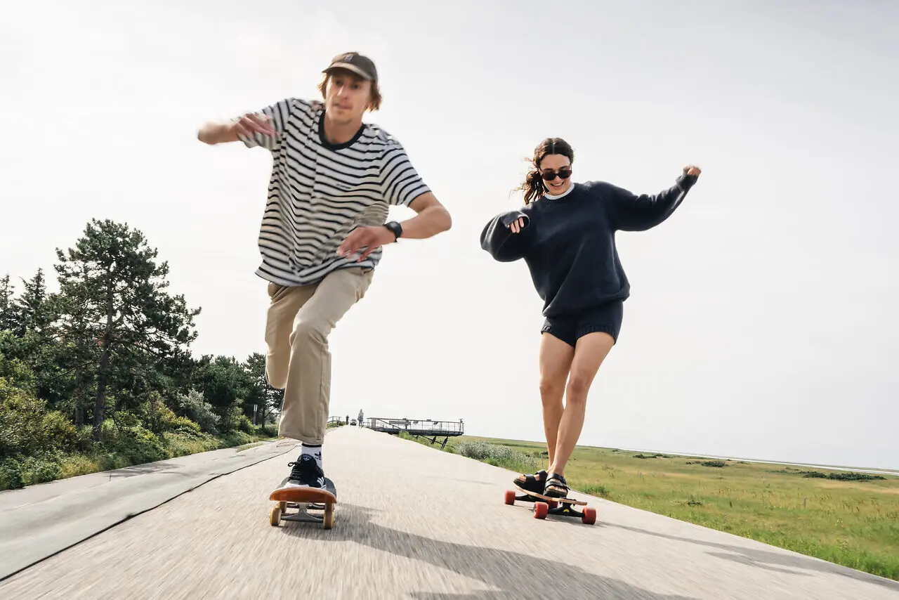 Longboards St. Peter-Ording Zwei Menschen fahren auf Longboards über Asphalt.