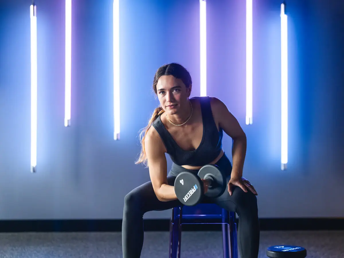Fitness Urban Nature St. Peter-Ording Eine Frau sitzt auf einer Hantelbank im Fitnessbereich des Urban Nature Hotels in St. Peter-Ording und stemmt eine Hantel.