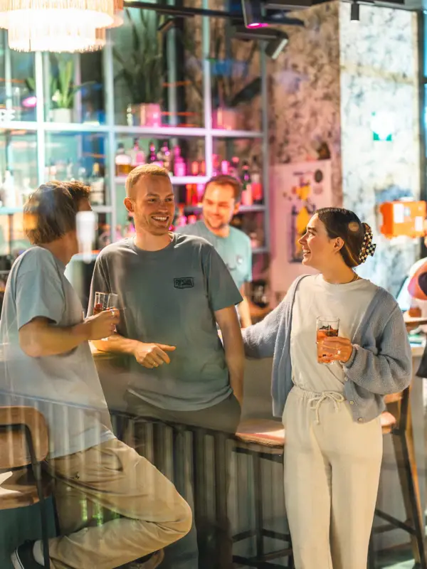 Mehrere Menschen stehen an einer Bar und unterhalten sich mit Getränken in der Hand.