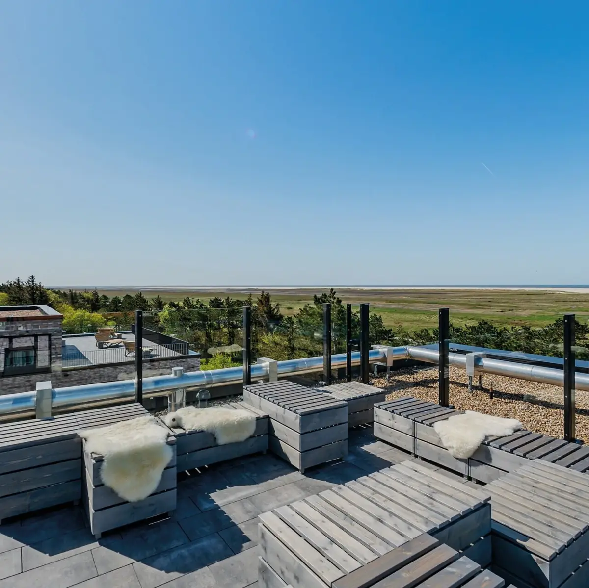 Eine Dachterrasse mit Holzmöbeln und einem tollen Ausblick über die Salzwiesen bis hin zur Nordsee von St. Peter-Ording.