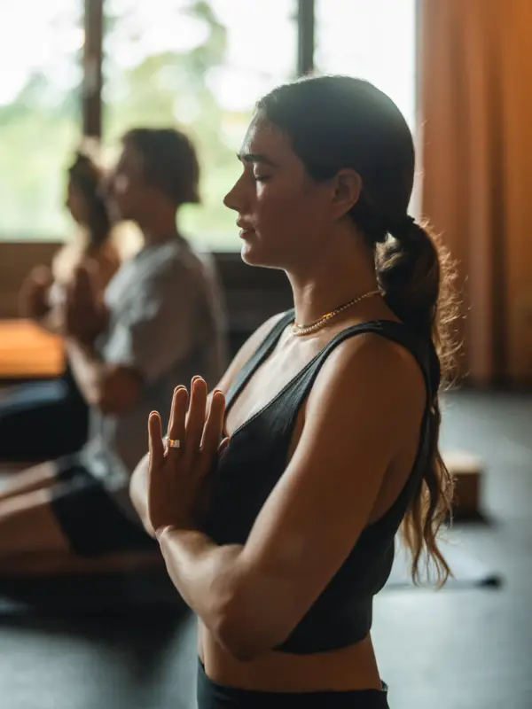 Eine Frau in einem schwarzen Top macht Yoga mit vor dem Körper zusammengelegten Händen.