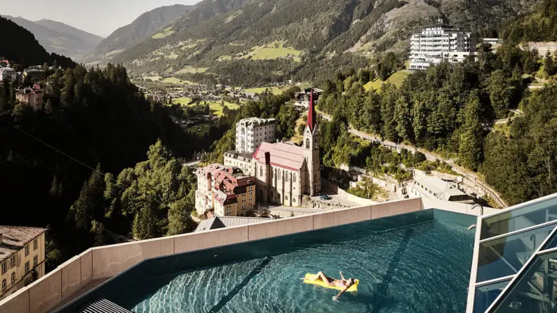 Eine Frau schwimmt auf einer gelben Luftmatratze auf dem Rooftop-Pool vom Urban Nature Badeschloss Bad gastein mit Blick in das Tal und die Berglandschaft.