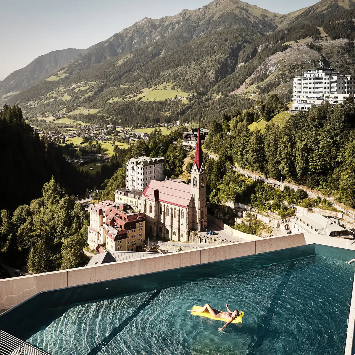 Das Urban Nature Hotel Bad Gastein mit einer Person im Rooftop-Infinity-Pool mit Blick auf die Berge.