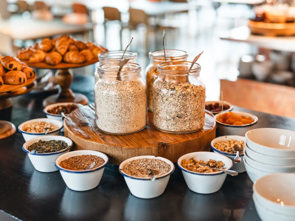 Müsli Frühstücksbuffet St. Peter-Ording Auf einem Buffet stehen mehrere Glasbehälter mit Müsli und davor sind viele Schälchen mit Nüssen und Toppings.