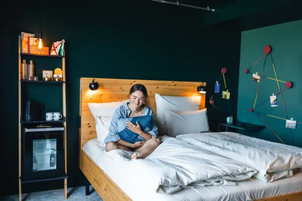 Eine Frau sitzt auf einem Bett in einem Zimmer im Urban Nature Hotel St. Peter-Ording und hält ein Kissen in ihren Armen.