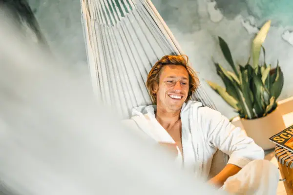 Ein Mann im Bademantel liegt lächelnd in einer Hängematte.