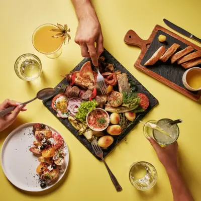 Bunte Auswahl an regionalen und mediterranen Spezialitäten auf einer gelben Tischplatte mit Brot, Getränken und Vorspeise