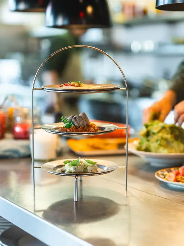 Eine Etagere mit drei Dips steht auf einer Küchen-Arbeitsplatte und im Hintergrund arbeitet ein Koch.