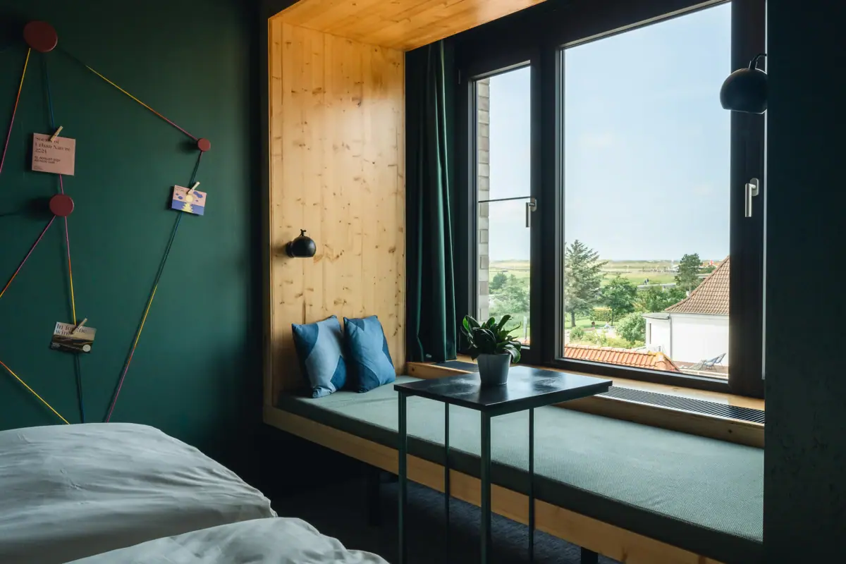 Ein Fenster mit einem Day-Bed und Blick auf die Salzwiesen von St. Peter-Ording. 