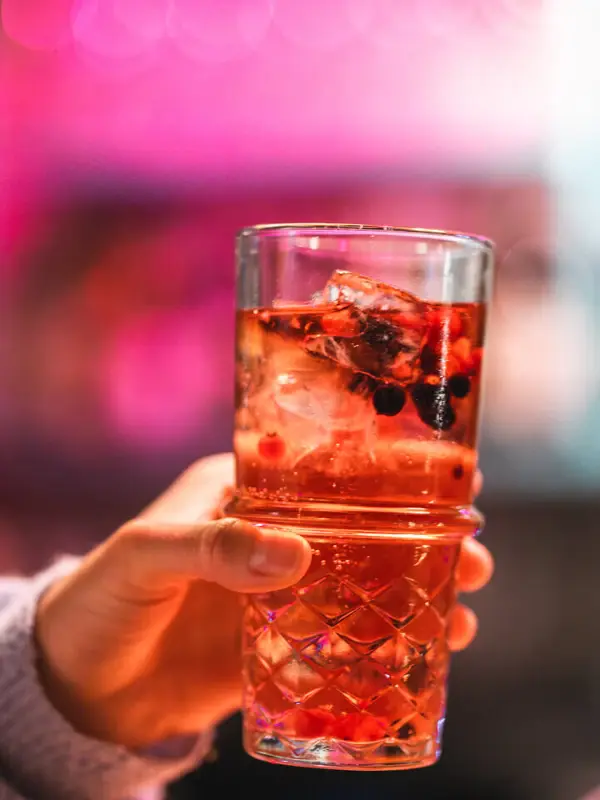 Eine Hand hält einen roten Drink in einem Glas mit Eiswürfeln und Beeren.