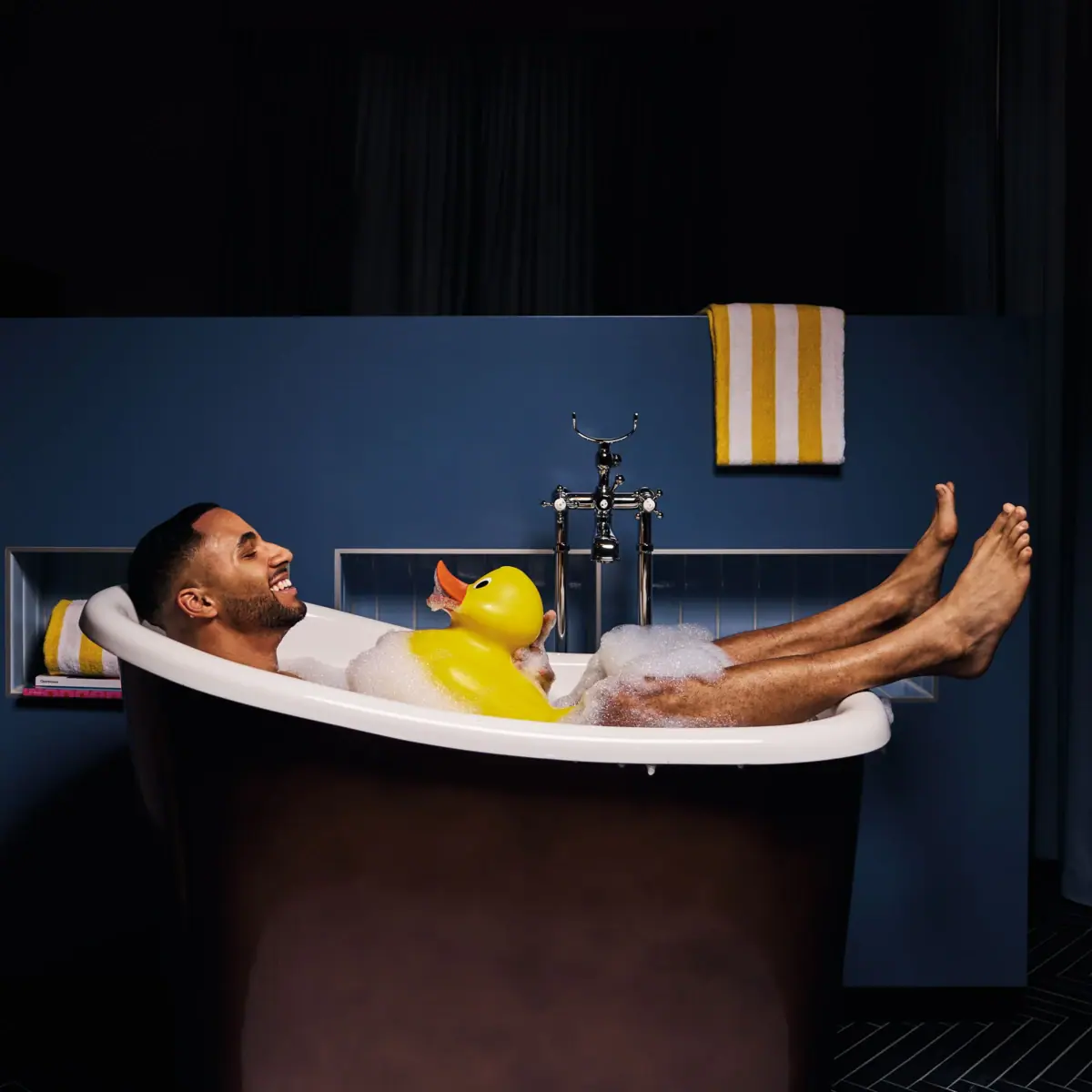 Ein Mann liegt in einer Badewanne mit einer Gummiente.