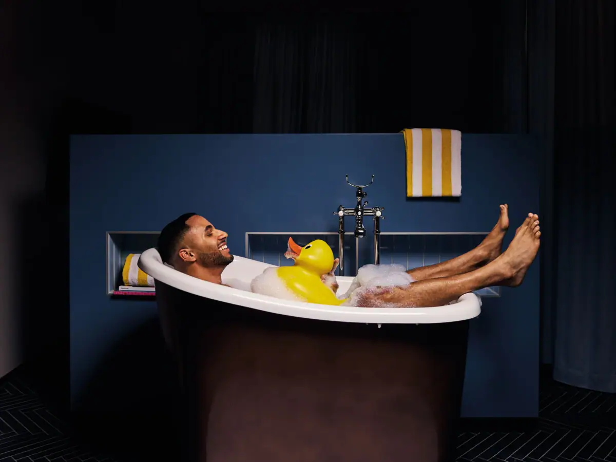 Ein Mann liegt in einer Badewanne mit einer Gummiente.