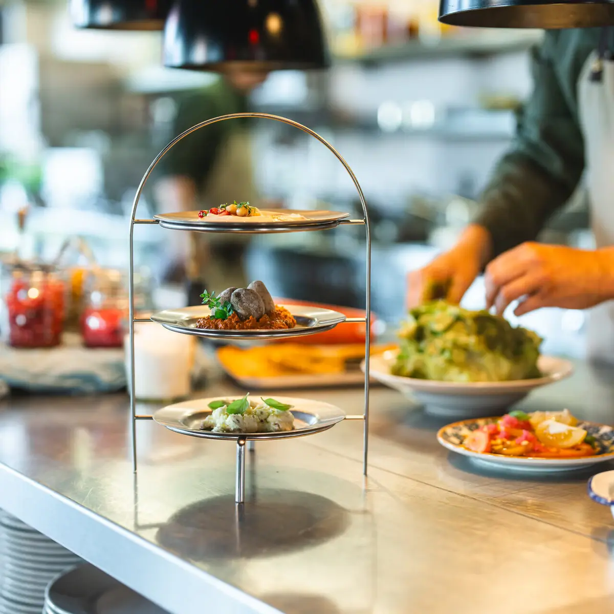 Eine Etagere mit drei Dips steht auf einer Küchen-Arbeitsplatte und im Hintergrund arbeitet ein Koch.