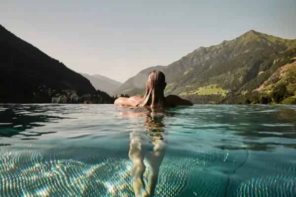 Rooftop Infinity Pool im Urban Nature Bad Gastein Eine Frau schwimmt in einem Pool mit Bergen im Hintergrund.