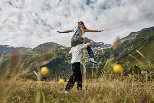 Wandern in Bad Gastein Ein Mann trägt eine Frau auf seinen Schultern in einem grasbewachsenen Feld.