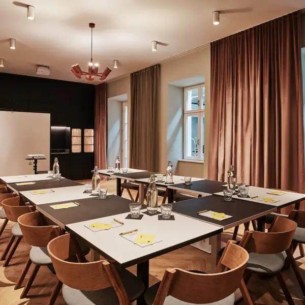 Ein Meetingraum mit einer U-Tafel, die mit Blöcken, Wassergläsern und Stiften eingedeckt ist. 