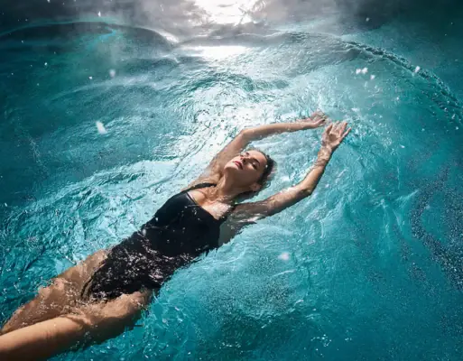 Wellness Bad Gastein Eine Frau in einem schwarzen Badeanzug schwebt im Pool.