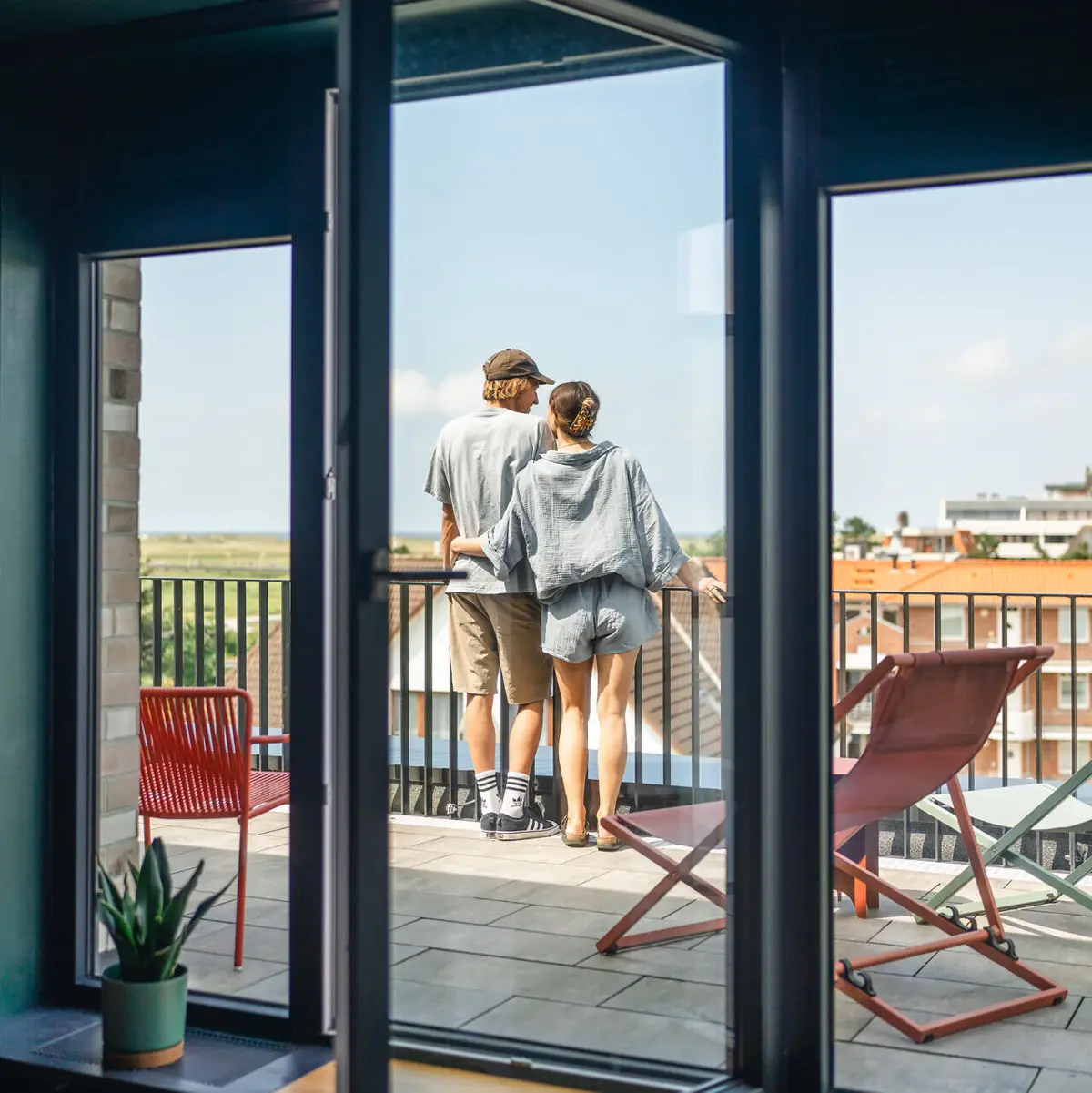 Zwei Personen stehen auf einem Balkon und blicken aus einem Fenster.