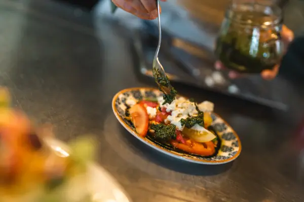 Ein Koch richtet ein Tellergericht mit Pfirsich und Burrata auf einer Küchenarbeitsplatte an.