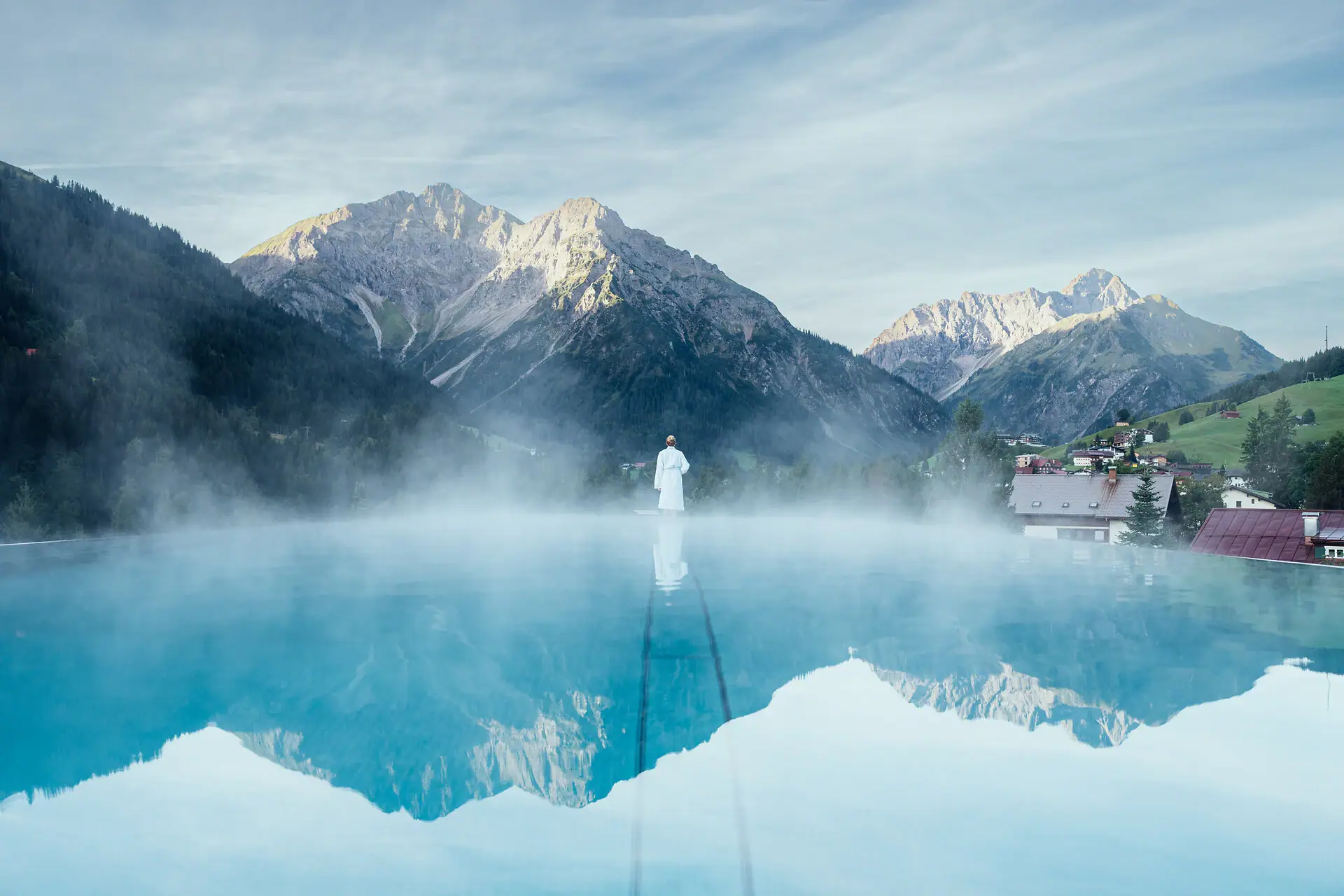 Eine Person steht in einem Pool mit Bergen im Hintergrund.