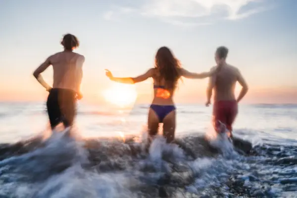 Eine Gruppe von Menschen springt ebi Sonnenuntergang in die Wellen der Nordsee.