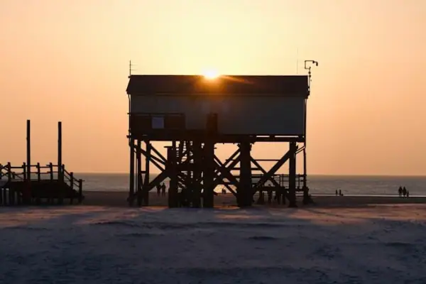 Ein Haus auf Stelzen am Strand von St. Peter-Ording bei Sonnenuntergang.