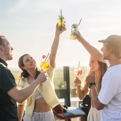 Eine Gruppe von Menschen steht auf der Rooftop Bar Scraper's Club St. Peter-Ording und stößt mit Getränken in der Hand an.