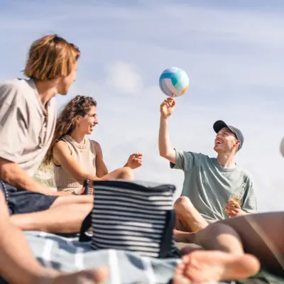 Eine Gruppe von Menschen sitzt am Strand und spielt mit einem Volleyball herum.