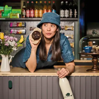 Eine Frau lehnt sich auf eine Theke und hält einen Muffin in der Hand.