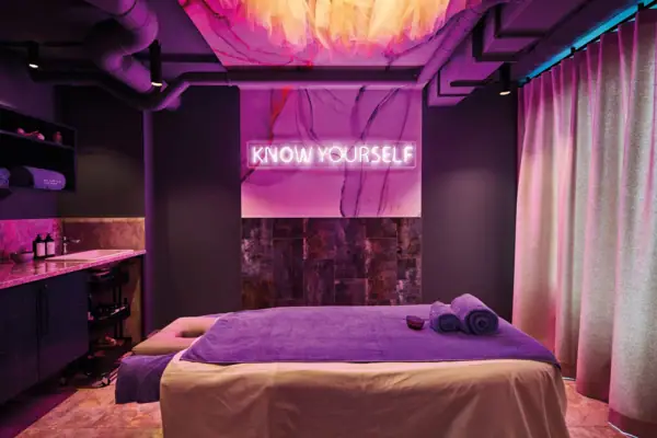 Lila Zimmer mit einer Massageliege und Handtuch im Urban Nature Hotel St. Peter-Ording.