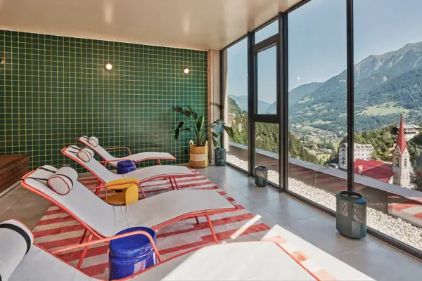 Moderner Ruheraum mit stylischen Liegen, großen Panoramafenstern und Blick auf die Berge und Kirche von Bad Gastein