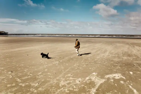 Ein Mann läuft mit einem Hund am Strand von St. Peter-Ording lang.