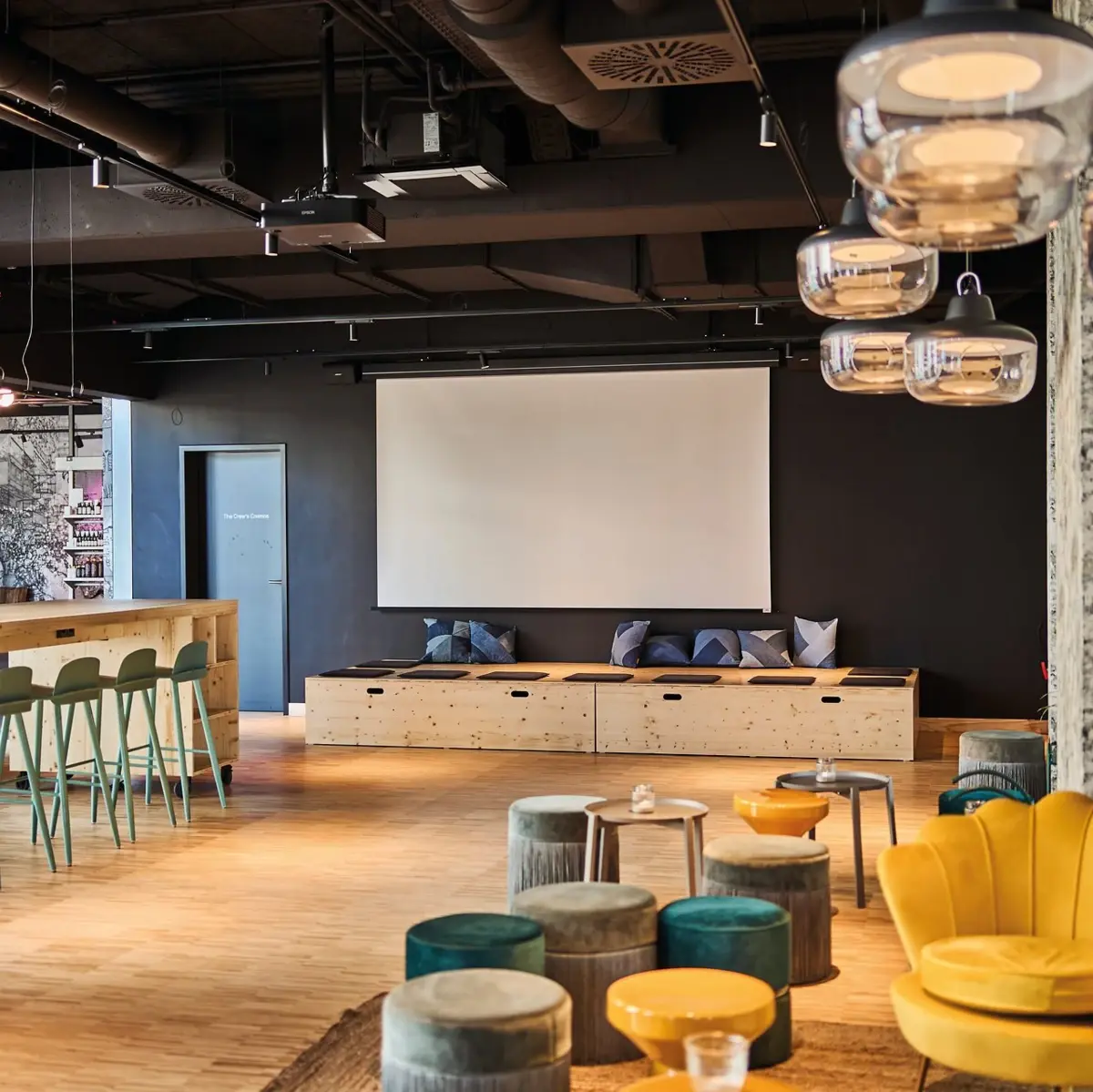 Multifunctional Space Ein offner Meetingspace mit einer Leinwand an der Wand.