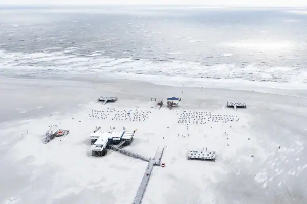 Weihnachten an der Nordsee Ein Pier mit Menschen darauf an einem verschneiten Strand im Winter.